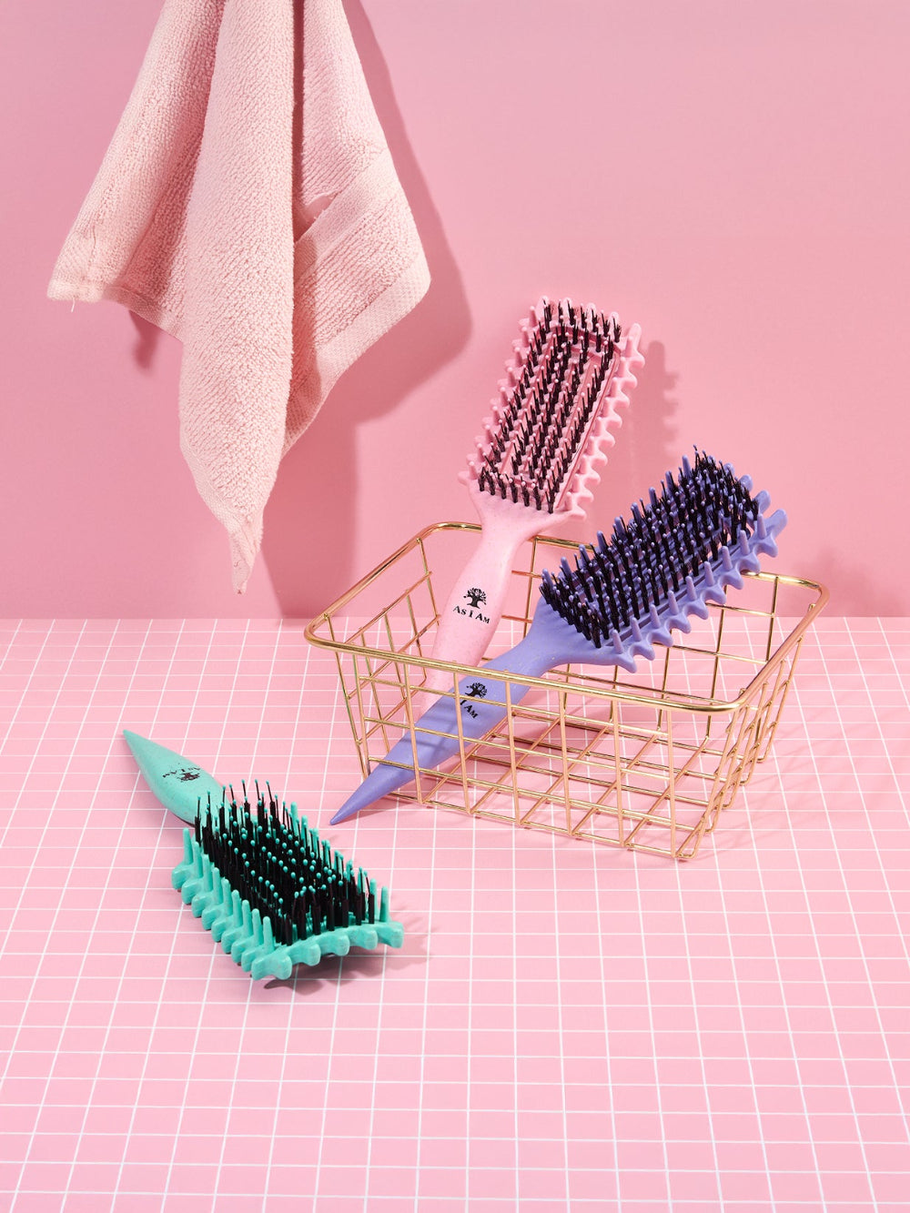 Trois brosses à cheveux de couleurs différentes sur un fond de grille rose avec un panier doré.