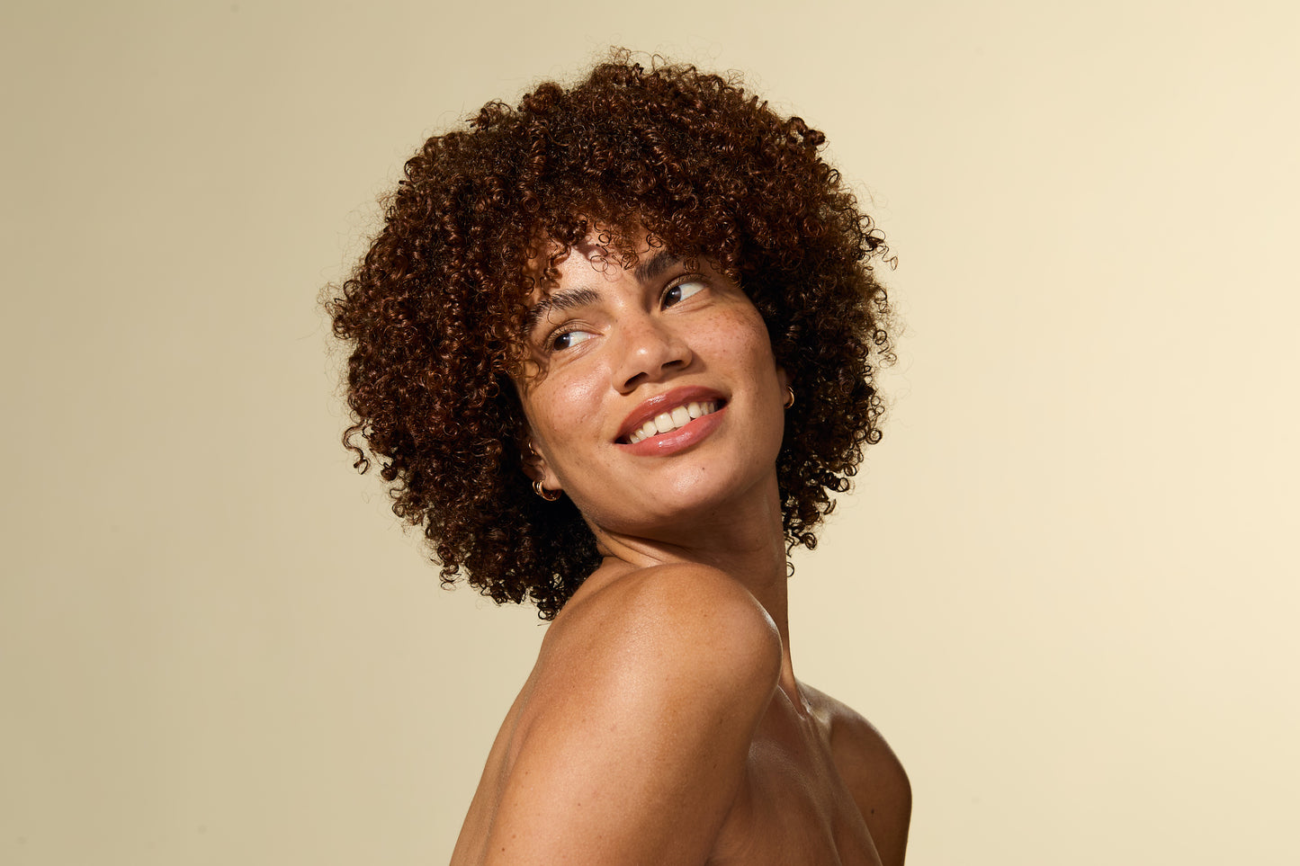 Femme aux cheveux bouclés souriant sur fond beige
