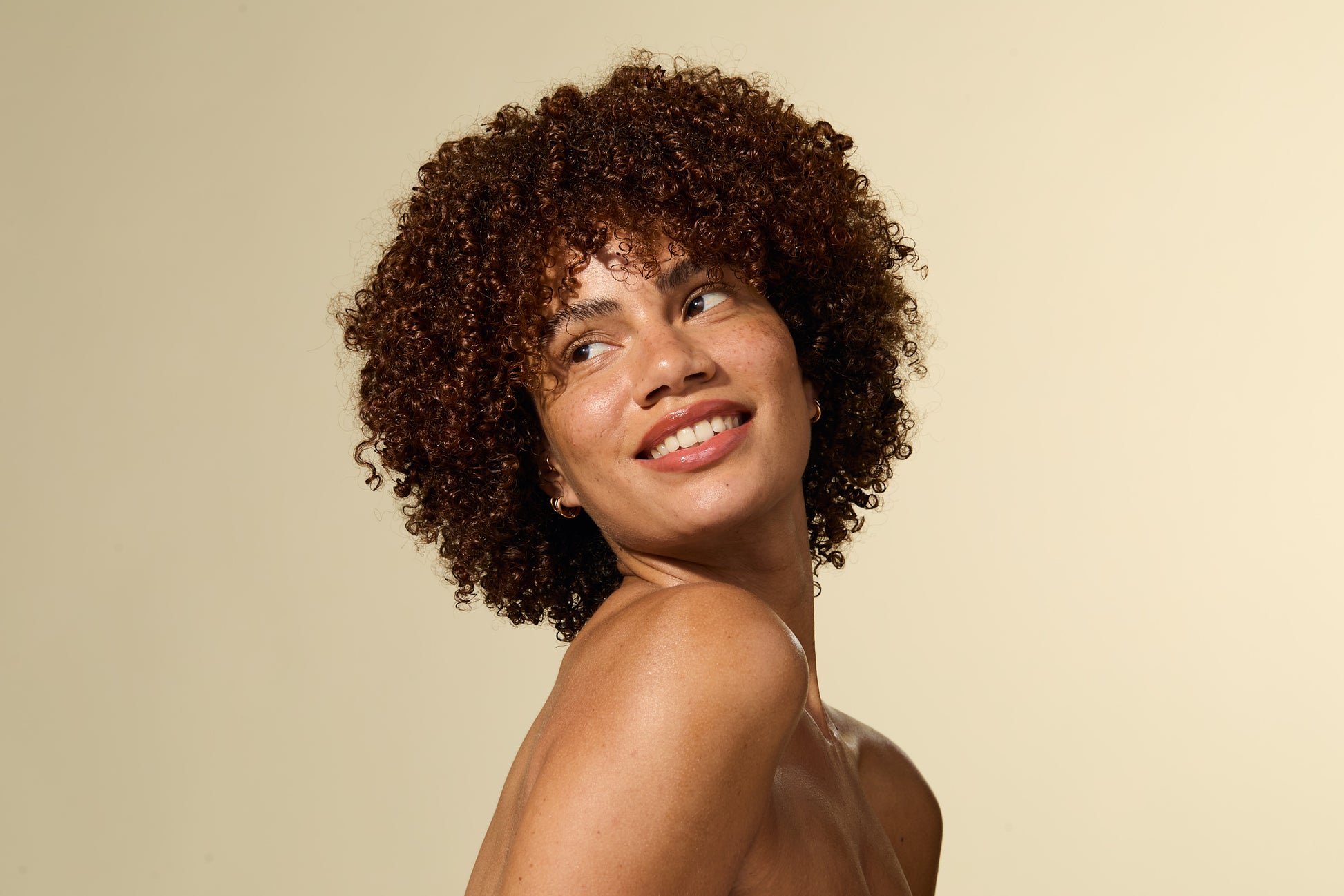 Femme aux cheveux bouclés souriant sur fond beige