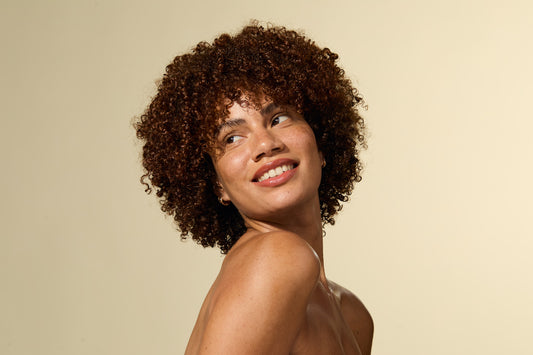 Femme aux cheveux bouclés souriant sur fond beige