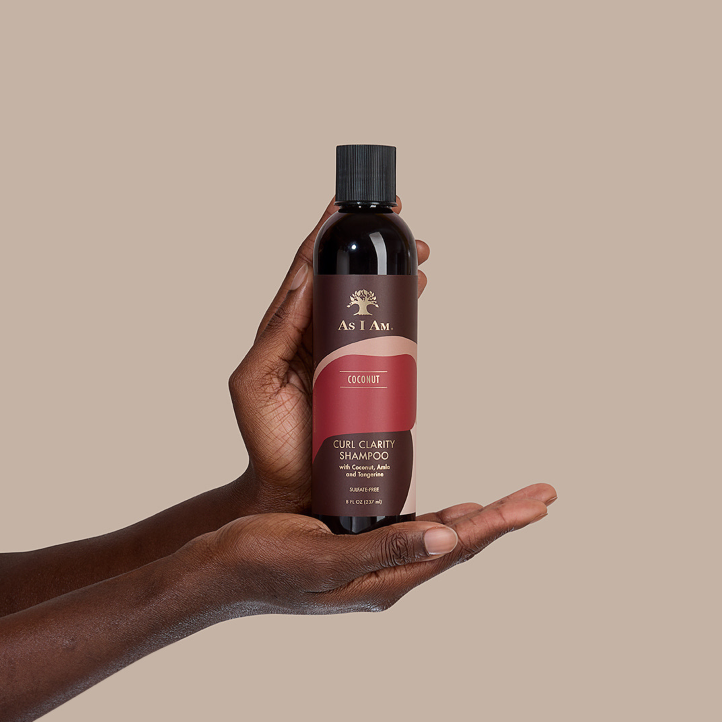 Main tenant un flacon de shampooing As I Am Coconut Curl Clarity sur fond beige