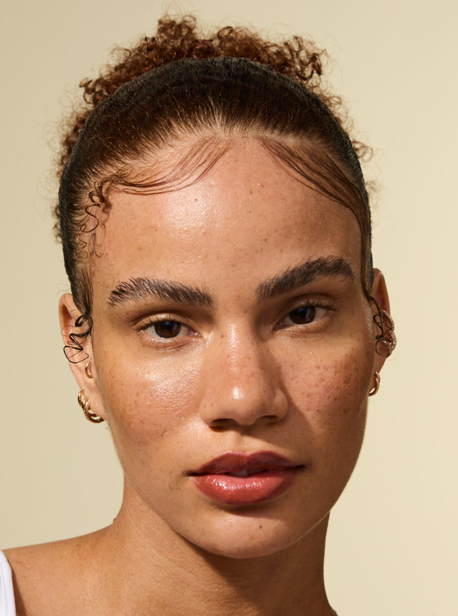 Modèle avec des bords lisses et posés et une coiffure soignée coiffée avec le bâton de cire au romarin AS I AM : les cheveux paraissent lisses, sans frisottis et fermement maintenus en place avec un fini d'apparence naturelle.