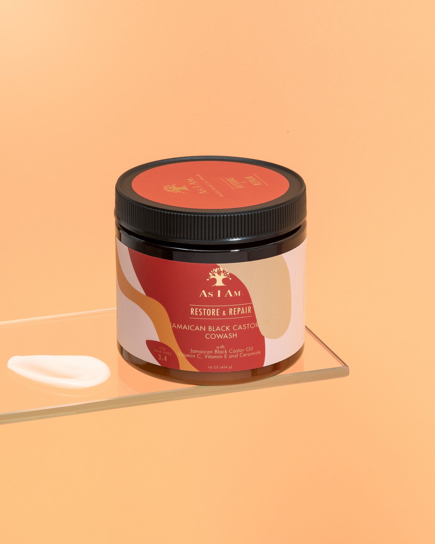 Un flacon de cowash à l'huile de ricin noire jamaïcaine avec une étiquette indiquant les détails du produit, placé sur une surface réfléchissante avec un fond orange uni.