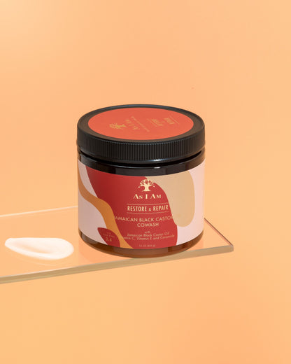 Un flacon de cowash à l'huile de ricin noire jamaïcaine avec une étiquette indiquant les détails du produit, placé sur une surface réfléchissante avec un fond orange uni.